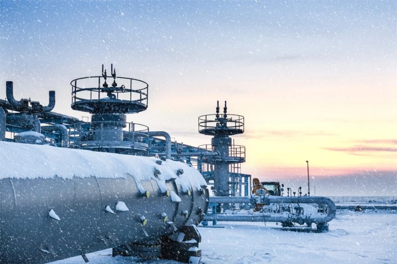 Snow-covered industrial automation equipment with pipes and processing towers at an Edmonton oil refinery at sunrise.