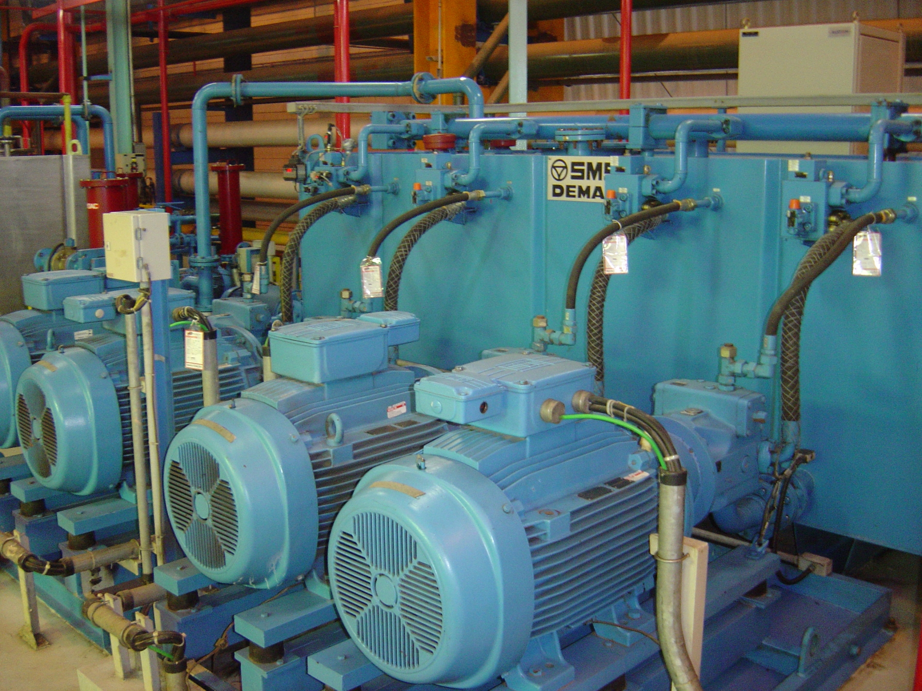 Electric motors connected to hydraulic pump systems in an industrial facility, tagged for maintenance tracking.