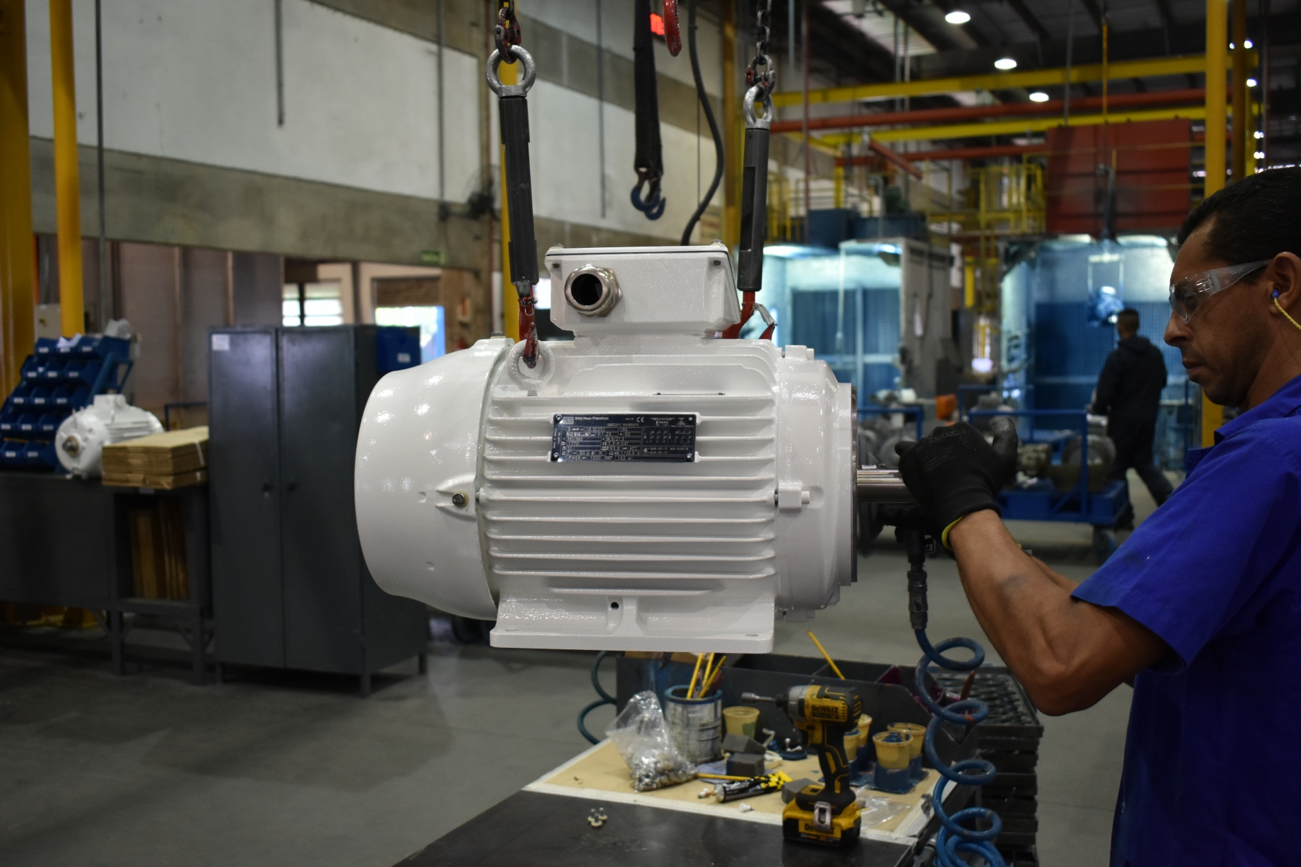 Technician performing preventive maintenance on a suspended electric motor inside an industrial facility.