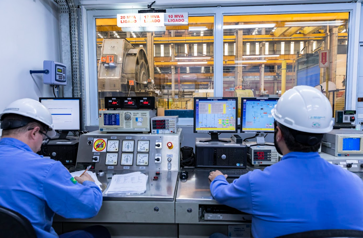 Engineers in a control room monitoring industrial motors and automation systems through computer interfaces and electrical control panels.