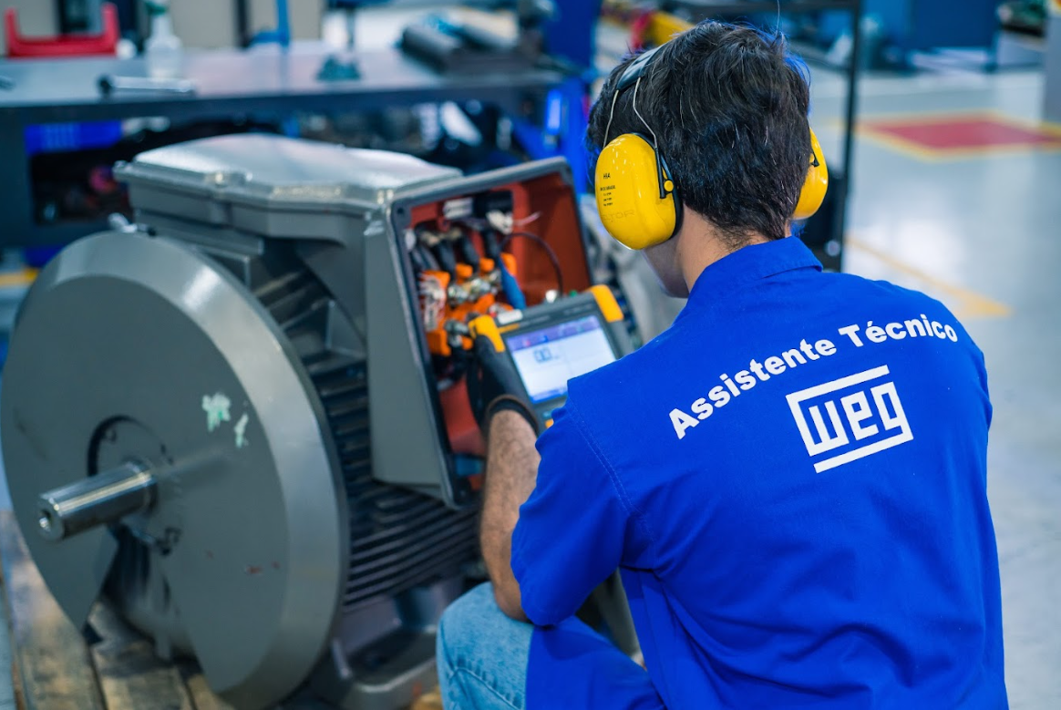 Technician performing motor maintenance inspection at a control station in a manufacturing facility.