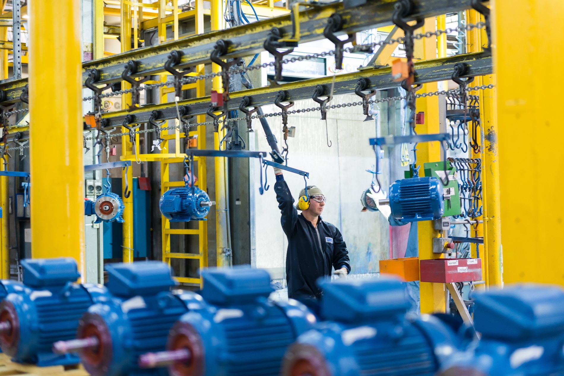 Technician guiding electric motors along an overhead conveyor system after painting.