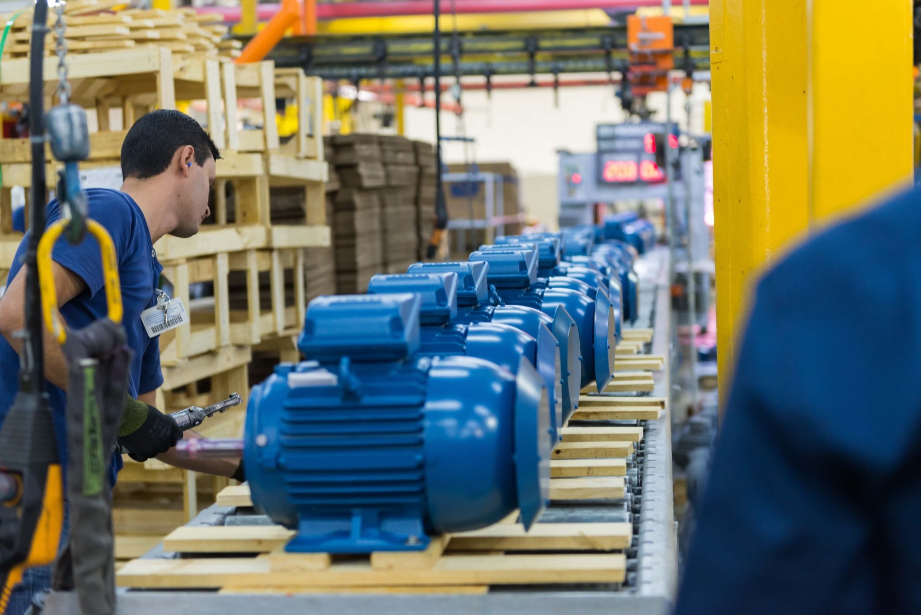 Technician inspecting blue electric motors on an industrial assembly line before shipment.