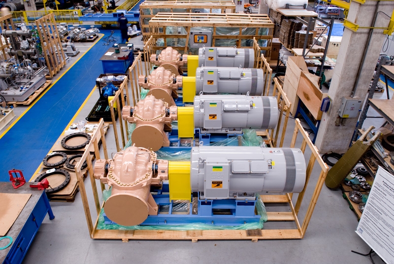 Large AC motors paired with industrial pumps staged on pallets inside a manufacturing facility.