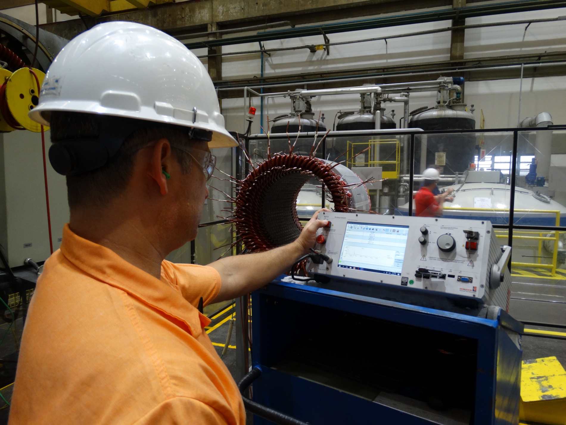 Technician in safety gear with oscilloscope at a testing bench performing quality control.